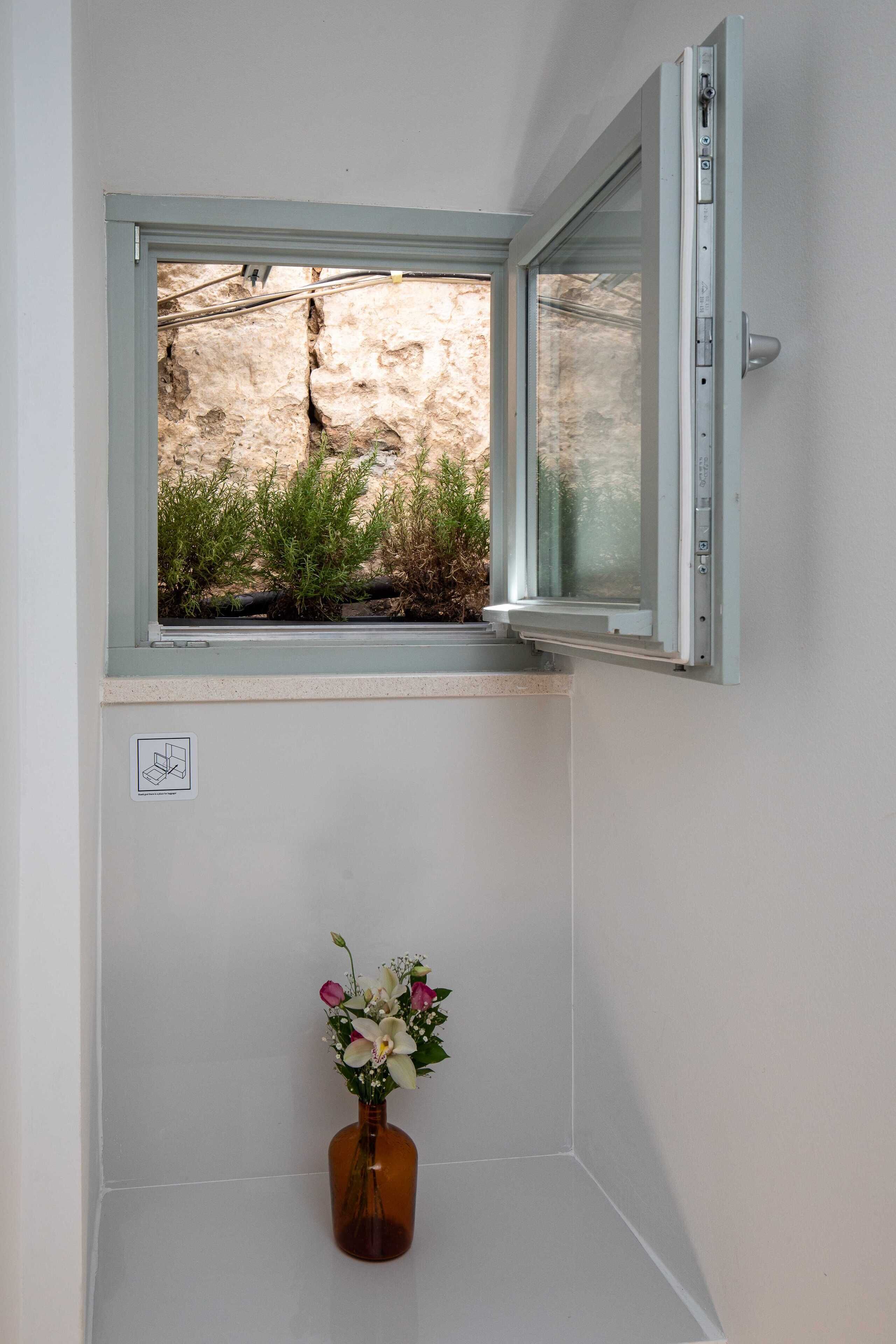 A bathroom with a window, a white wall, and a vase with flowers.