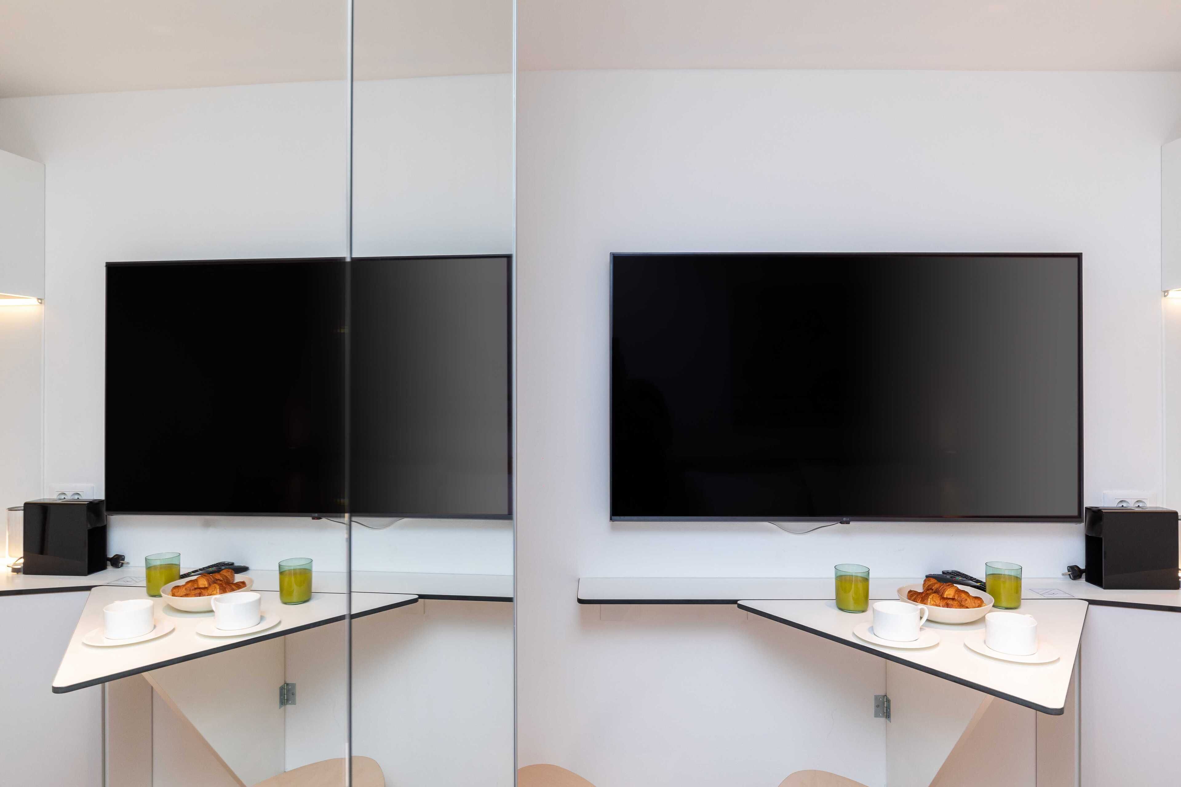 A modern room with a large flat-screen TV, a glass partition, and a breakfast setup with cups and a bowl of food.
