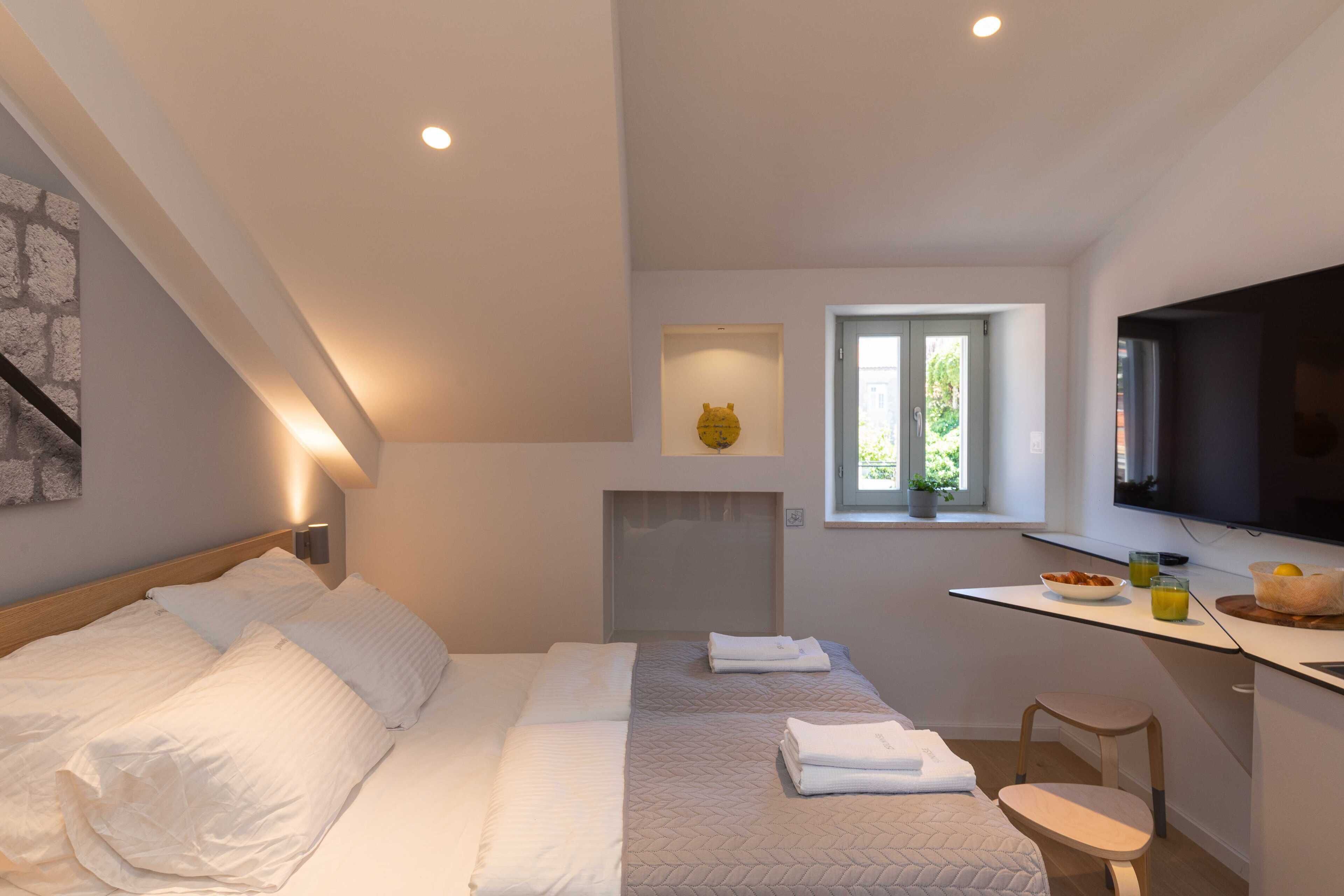 Un dormitorio moderno con una cama, mesitas de noche, un televisor y una ventana pequeña.