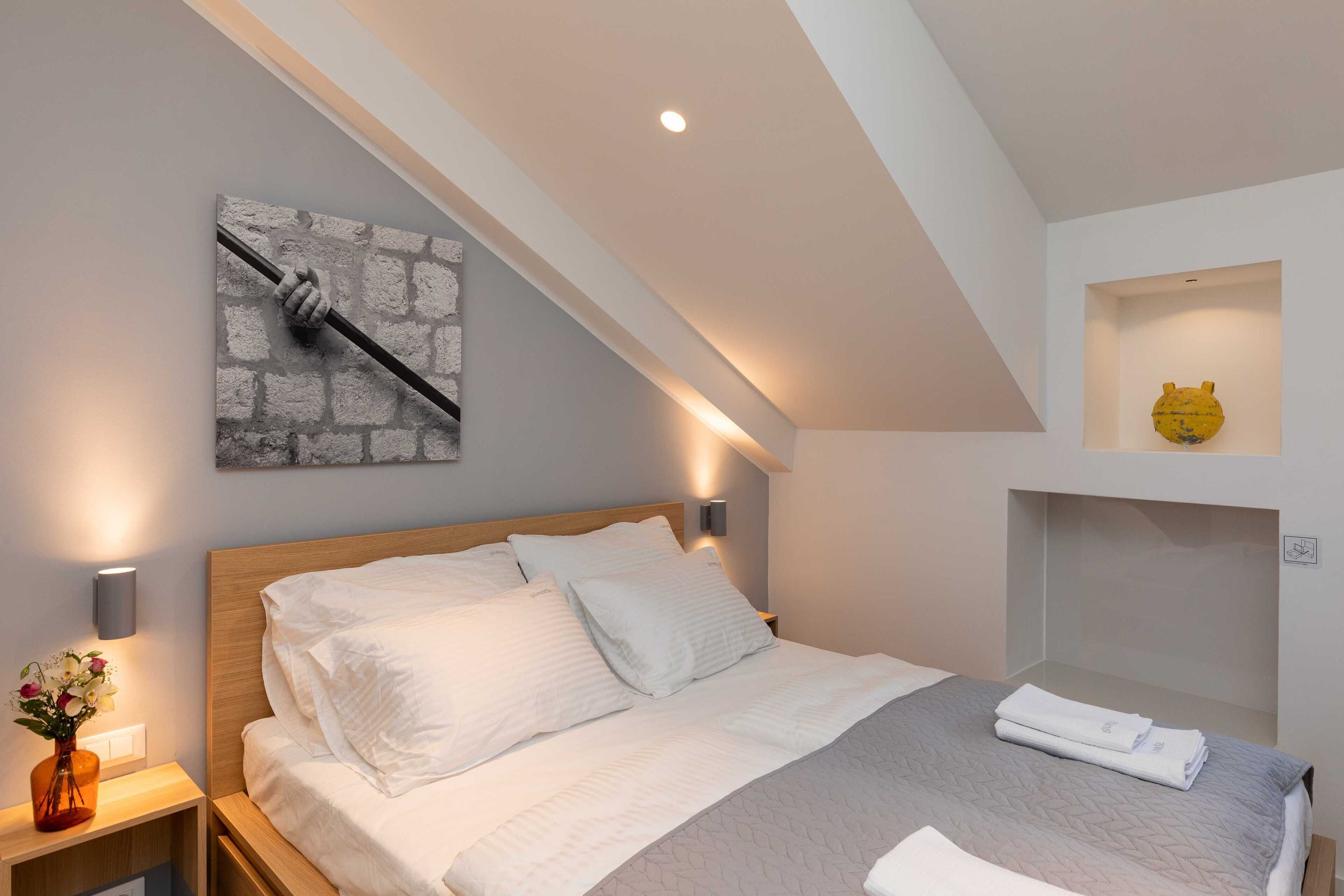 Ein ordentlich eingerichtetes Schlafzimmer mit einem Holz-Kopfteil, einem Bett mit weißer Bettwäsche, einem Wandbild und einer kleinen Ablage mit einem dekorativen Gegenstand.