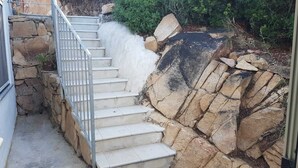 Escadaria de concreto com grades de metal que sobe um declive rochoso.