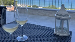 Duas taças de vinho sobre uma mesa de tear, com um candeeiro e vista para o mar e montanhas.