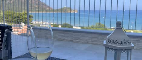 Two wine glasses on a woven table with a lantern and a view of the sea and mountains.