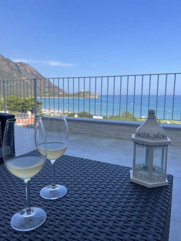 Two wine glasses on a woven table with a lantern and a view of the sea and mountains.