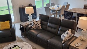 A modern living room with a leather sofa, a coffee table, and a dining area with a table and chairs. - 3/2 IN THE VILLAGE OF ST. CATHERINE GAS GOLF CART, CLOSE TO SAWGRASS GROVE (Wildwood)