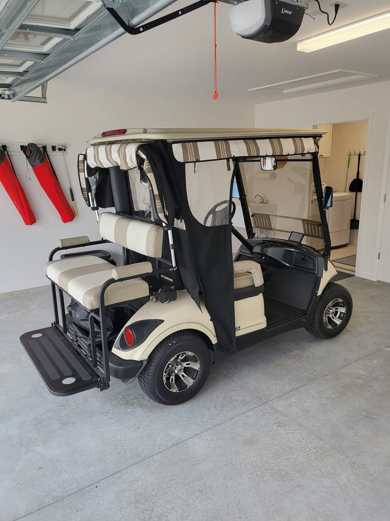 A golf cart in a garage with a ceiling fan, a washing machine, and a door in the background.