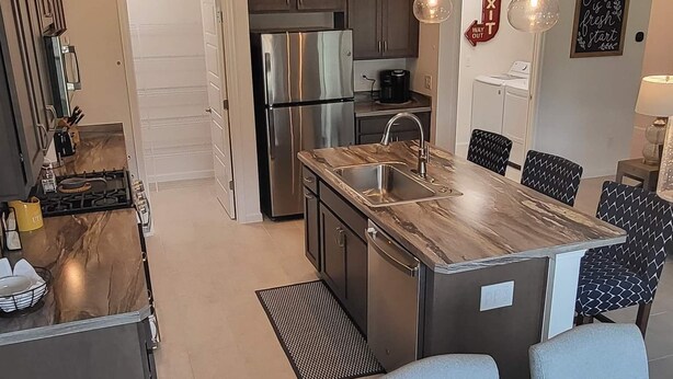 A modern kitchen with stainless steel appliances, a central island with a sink, and a dining area with a marble table and woven placemats. - 3/2 IN THE VILLAGE OF ST. CATHERINE GAS GOLF CART, CLOSE TO SAWGRASS GROVE (Wildwood)