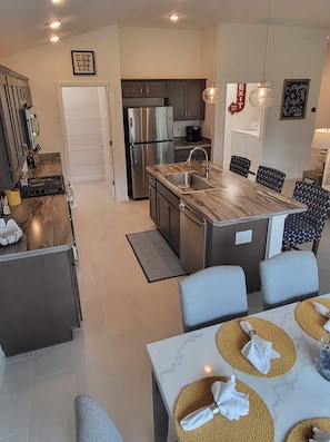 Uma cozinha moderna com eletrodomésticos de aço inoxidável, uma ilha central com pia e uma área de jantar com mesa de mármore e jogos americanos trançados.
