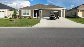 A single-story house with a garage, a driveway, and a golf cart parked in front. - 3/2 IN THE VILLAGE OF ST. CATHERINE GAS GOLF CART, CLOSE TO SAWGRASS GROVE (Wildwood)