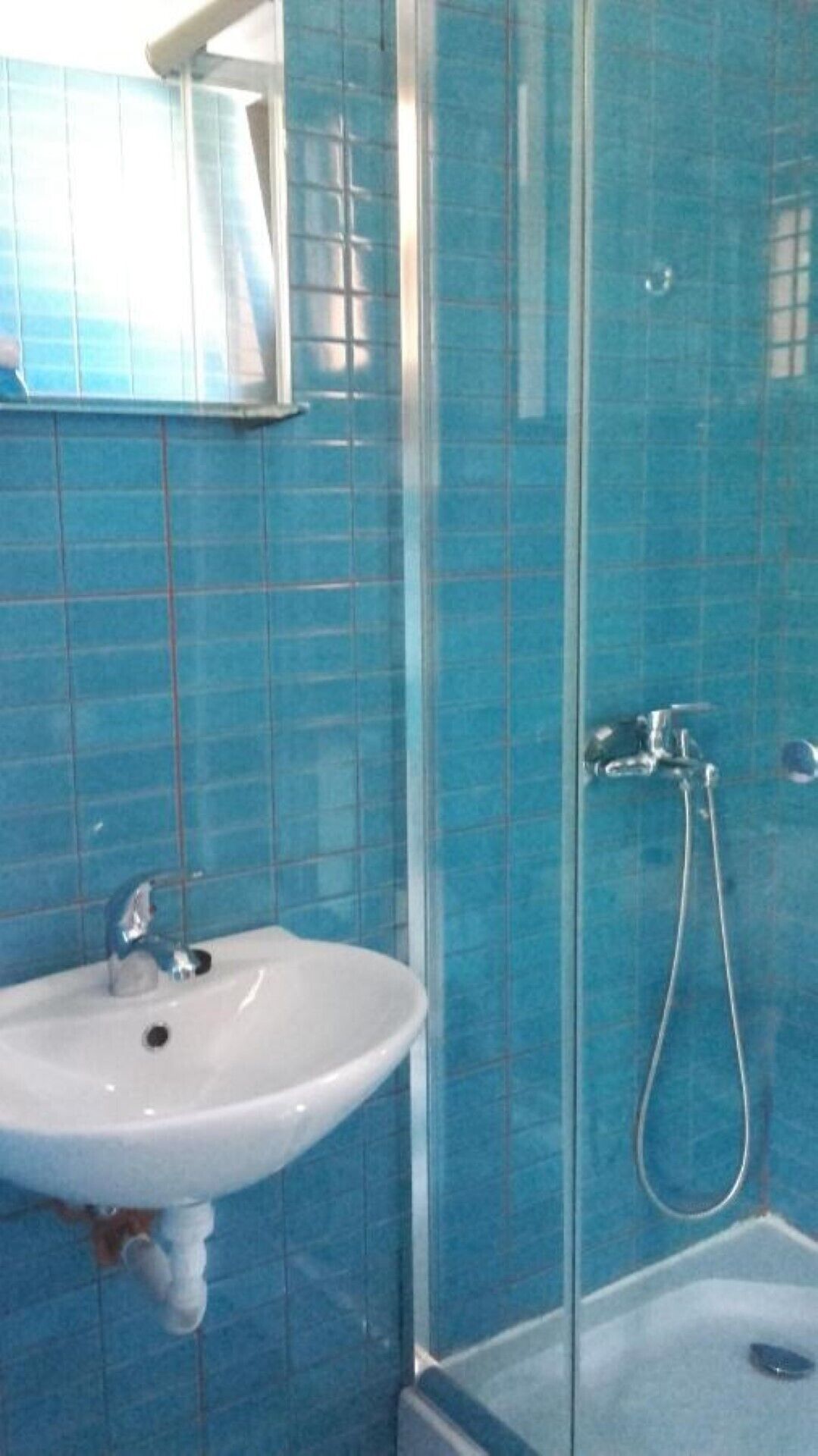 Un baño con un lavabo blanco, un espejo y una zona de ducha con azulejos azules.
