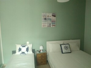 A bedroom with two beds, a wall clock, a small table, and a framed collage on the wall.