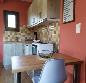 A compact kitchen with a wooden table, a white chair, and a tiled backsplash.