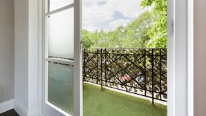 A view from a room with a large window overlooking a green lawn and a black metal fence. - The Fulham Penthouse (London)