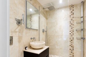 A modern bathroom with a large mirror, a round sink, and a shower with a glass door. - The Fulham Penthouse (London)