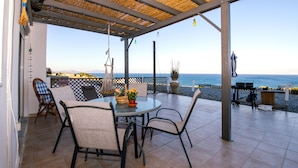 Une terrasse couverte avec une table ronde et des chaises, donnant sur une plage.
