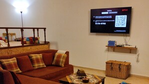 Un salon comprenant un canapé, des poufs, une table basse et un téléviseur à écran plat fixé au mur.