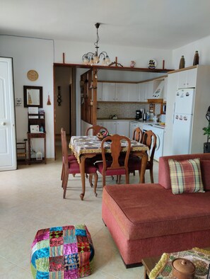 A cozy living room with a red sofa, a colorful quilt, and a dining area with wooden chairs and a patterned tablecloth.