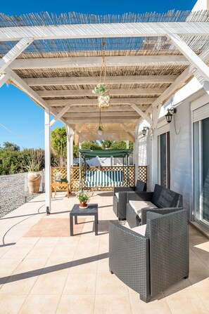 A covered outdoor seating area with wicker furniture, a hanging plant, and a view of the surrounding landscape.