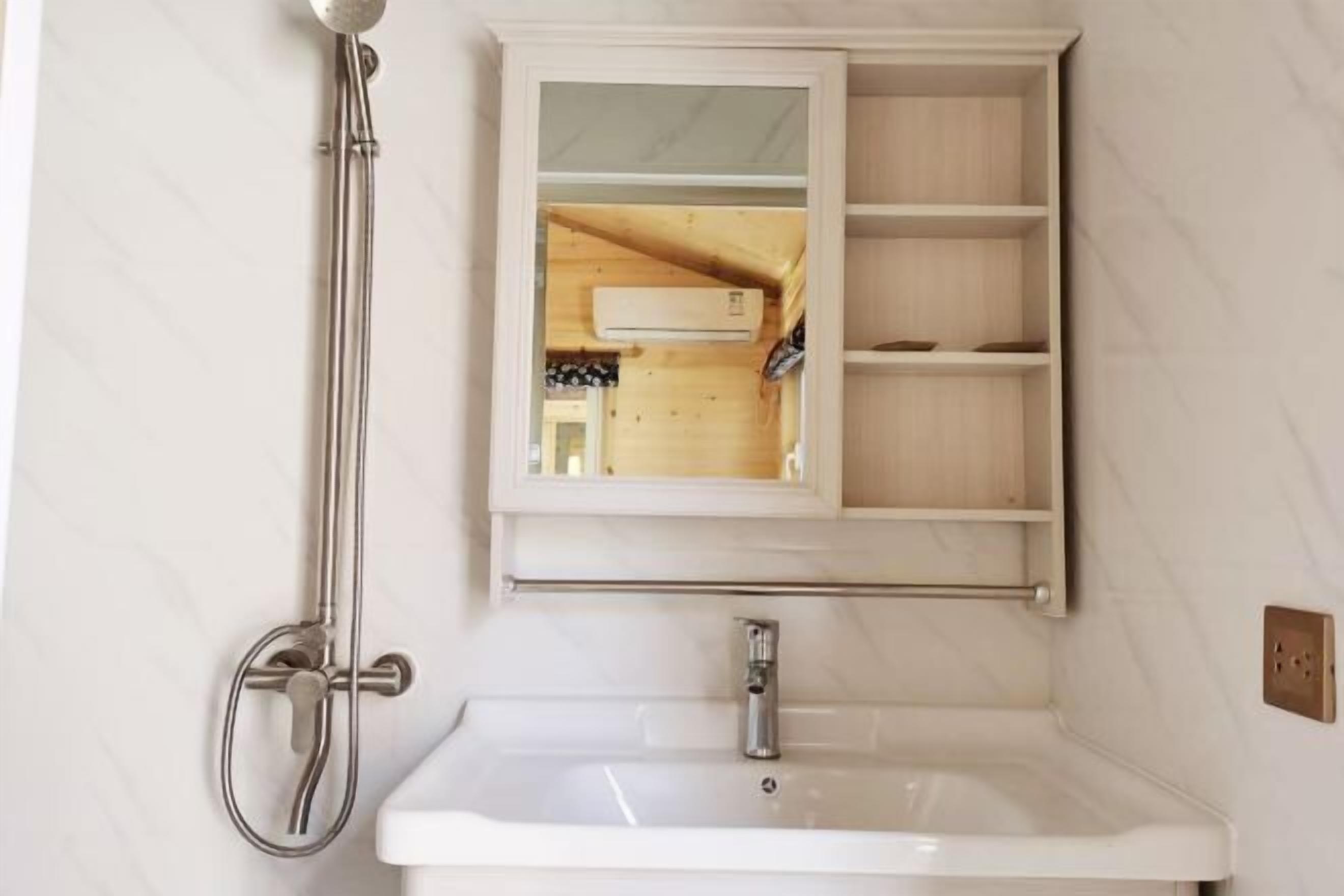 A bathroom with a white sink, a shower, and a wooden cabinet with open shelves.