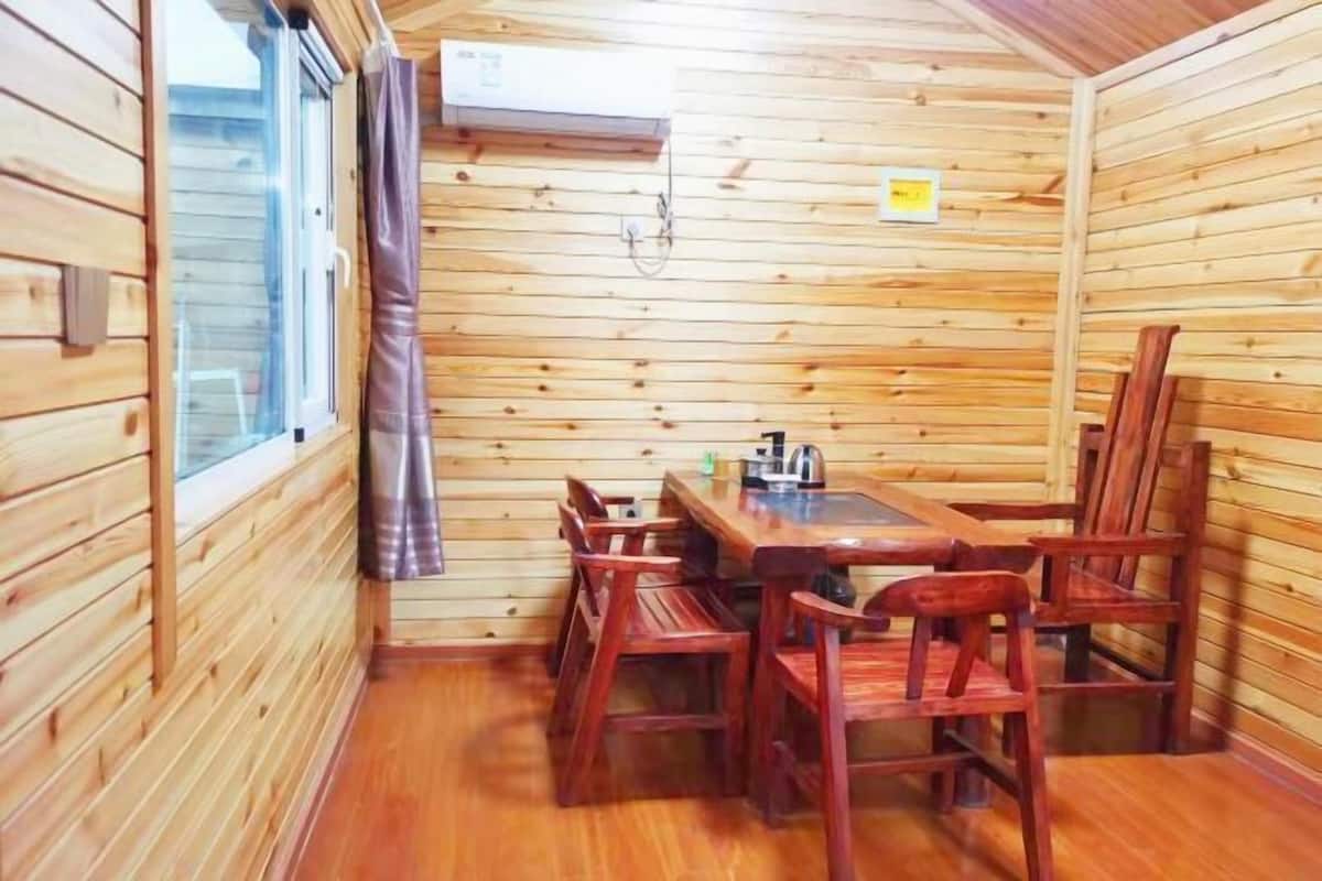 L’intérieur d’une cabane en bois comprend une table à manger et des chaises, une fenêtre avec des rideaux et un appareil de climatisation.