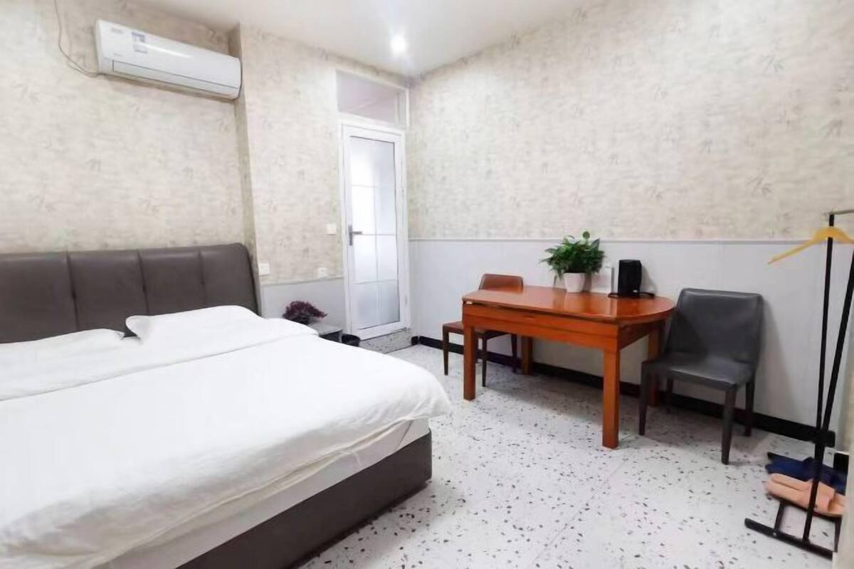 Une chambre d’hôtel avec un lit, une petite table sur laquelle est posée une plante, une chaise et un porte-manteau.