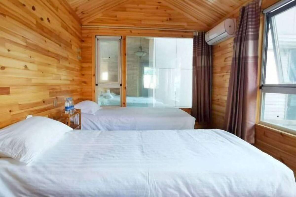 Une chambre dans un chalet en bois, avec deux lits, une porte-fenĂŞtre coulissante donnant sur un balcon et un appareil de climatisation.