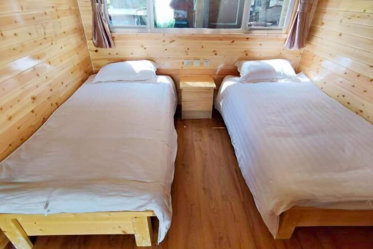 Une cabine avec deux lits en bois, une petite table de chevet en bois et une fenĂŞtre avec des rideaux.