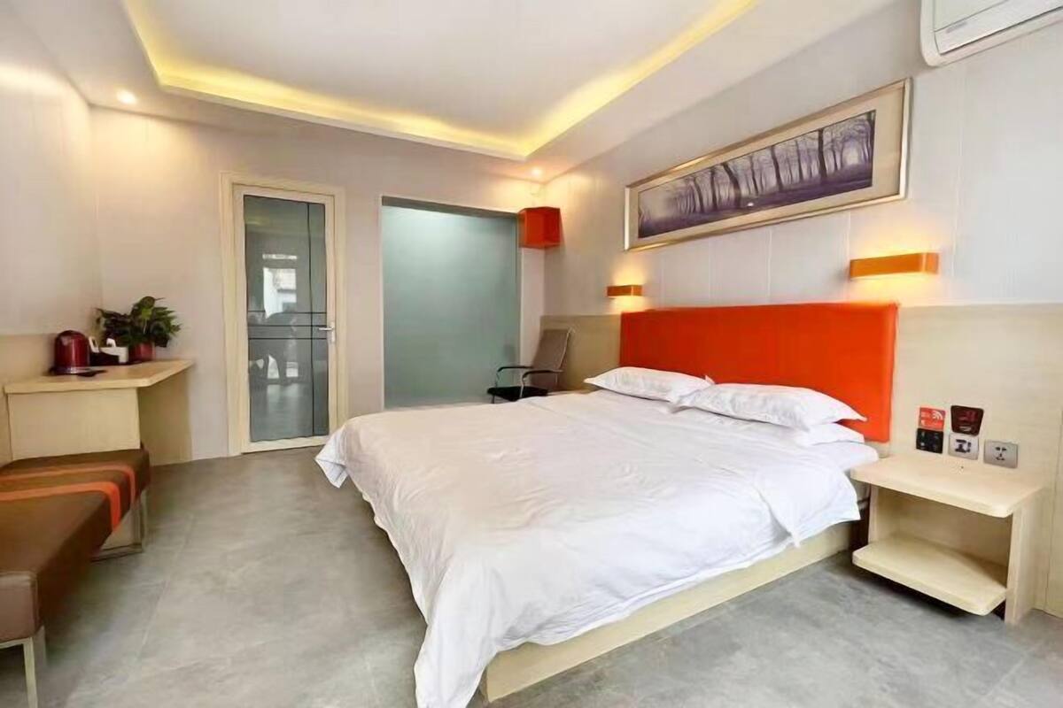 Une chambre d’hôtel moderne, dotée d’un grand lit, d’une table de chevet, d’une chaise, d’un petit bureau et d’une porte donnant sur un balcon.