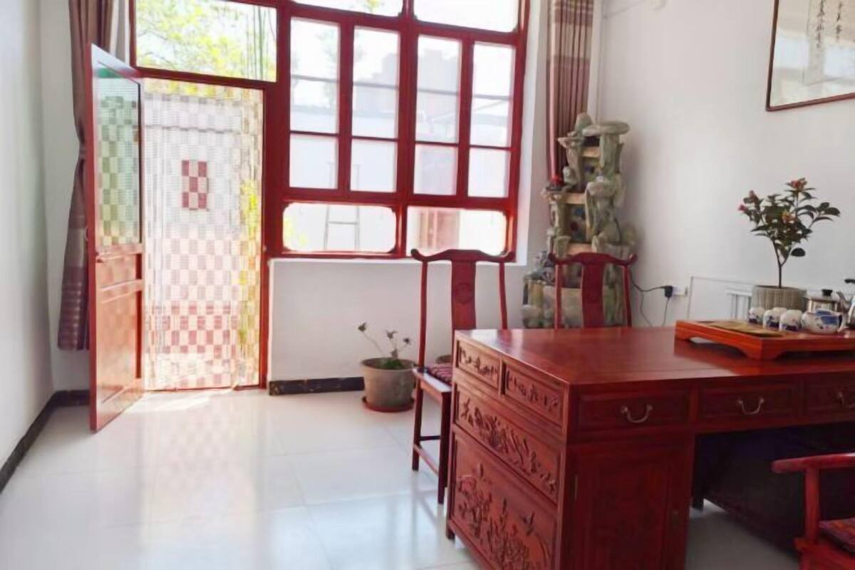 Une pièce avec un bureau en bois, une chaise, une plante en pot et une fenêtre donnant sur l’extérieur.
