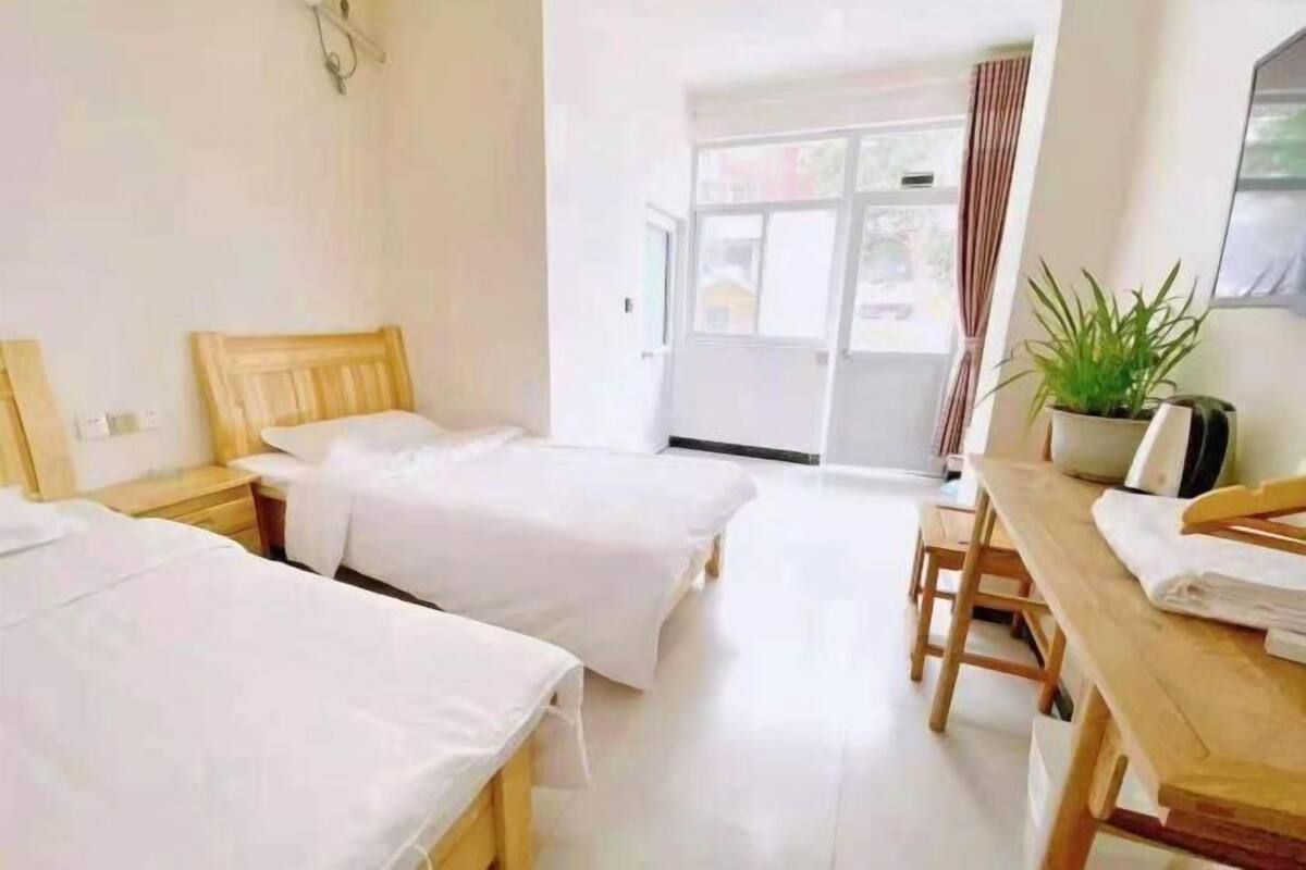 Une chambre d’hôtel avec deux lits simples, un bureau en bois, une chaise, une plante en pot et une porte-fenêtre coulissante donnant sur un espace extérieur.