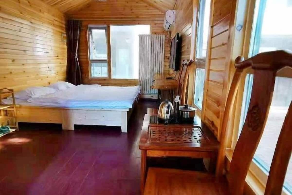 Une pièce de cabane en bois comprenant un lit, une table avec une bouilloire et une fenêtre.