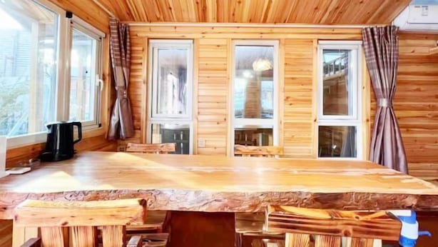Un intérieur en bois, avec de grandes fenêtres, une table en bois et des rideaux.