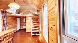 L’intérieur d’une cabane en bois, avec un lit en mezzanine, des étagères en bois et une grande fenêtre.