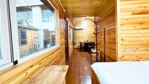 Un couloir étroit en bois, avec un lit sur le côté droit et une table et des chaises au centre.