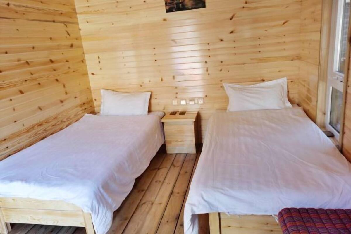 Une chambre dans un chalet en bois, avec deux lits simples, un petit banc en bois et une fenĂŞtre.