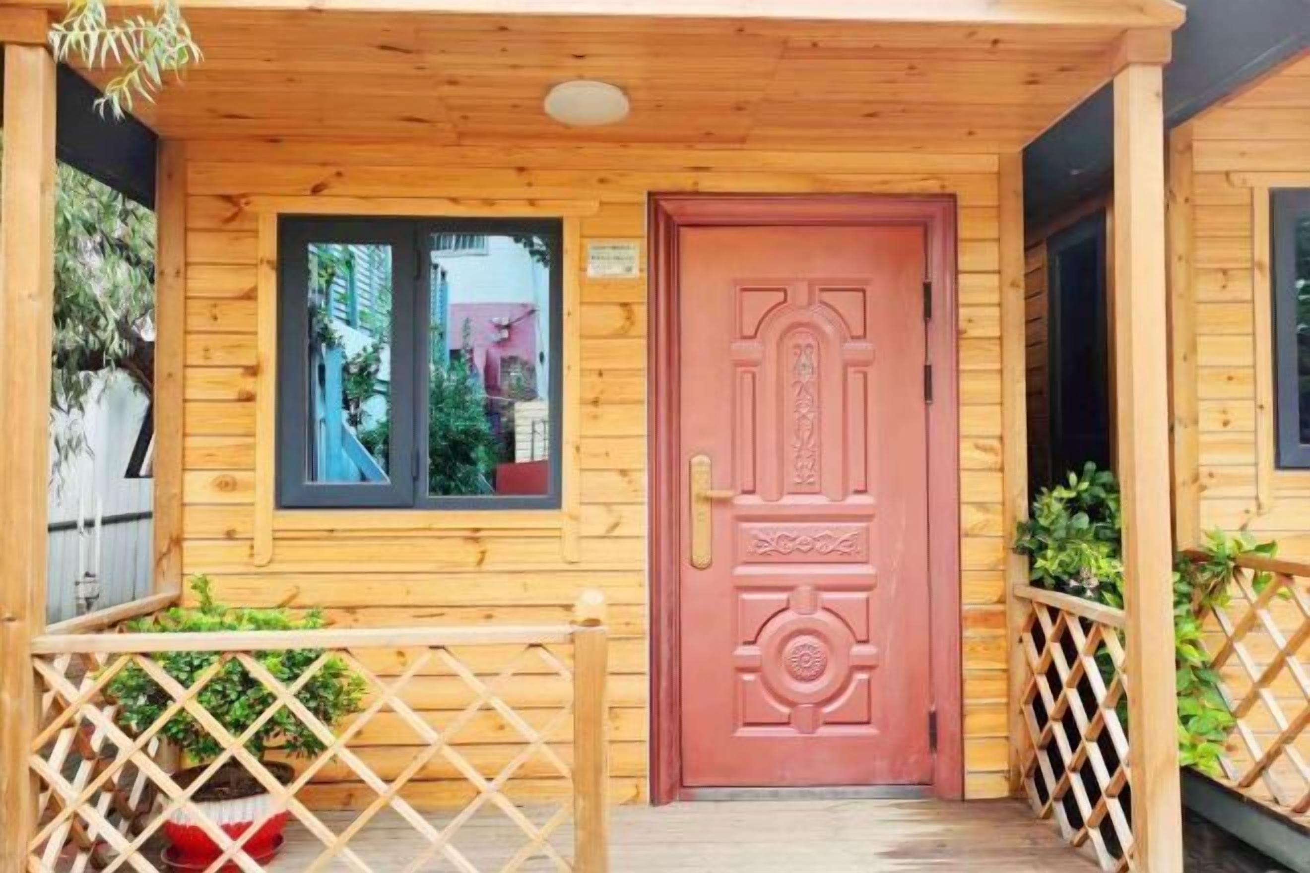 Une cabane en bois avec une porte rouge, une fenêtre et une balustrade en bois.