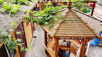 A wooden gazebo with a sloped roof, surrounded by a garden with climbing plants.
