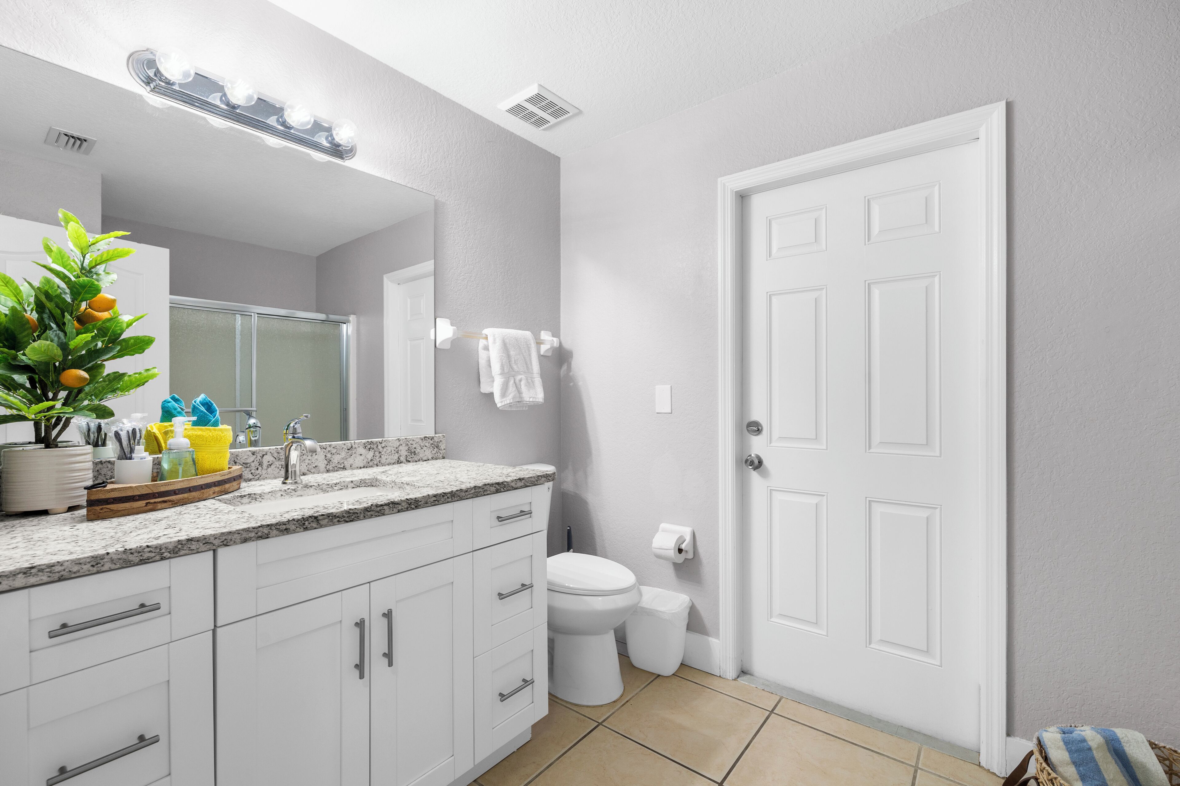 A modern bathroom with a white sink, mirror, and toilet. There is a potted plant on the counter and a towel rack on the wall.