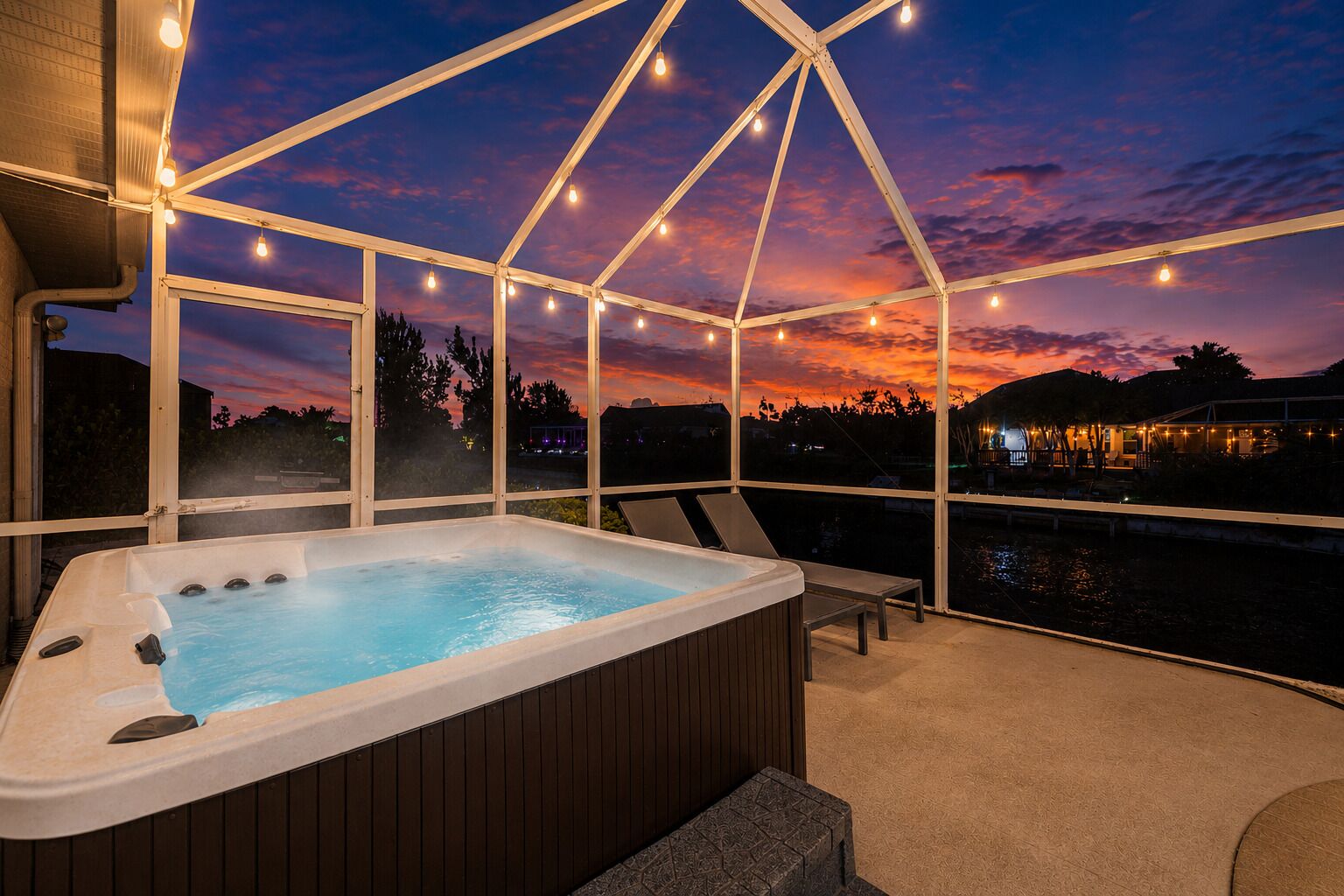Un bain à remous avec vue sur un coucher de soleil se reflétant sur une étendue d’eau, entouré d’une terrasse couverte.