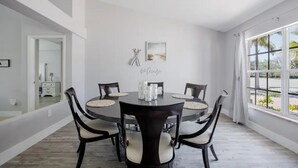 Un coin repas comprenant une table ronde, six chaises et une vue sur l’extérieur grâce à de grandes fenêtres.