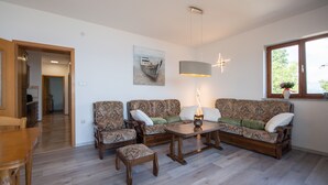 A living room with a sofa set, a coffee table, and a dining table. There is a painting on the wall and a window with a view of the outdoors. - Bela Vista 4 (Bregi)