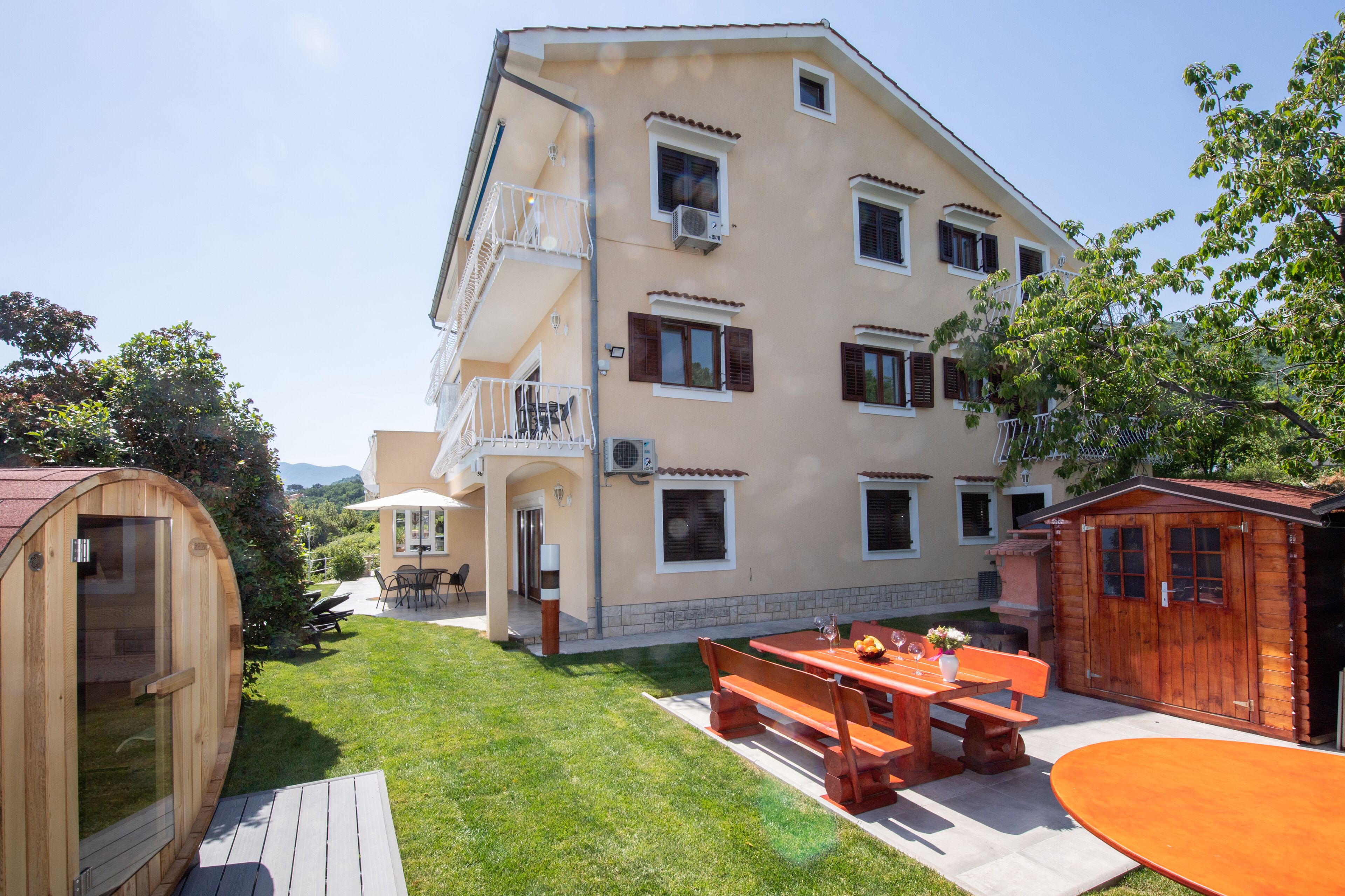 A two-story building with a balcony, a wooden sauna, and a patio with a table and benches.