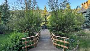 A wooden bridge leading to a building surrounded by trees and a clear sky. - Keystone Ski area, Epic mountains views, Ground floor condo, short walk to lift  (Keystone)