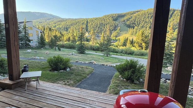 A wooden deck with a barbecue grill, a bench, and a view of a mountainous landscape with a house in the distance. - Keystone Ski area, Epic mountains views, Ground floor condo, short walk to lift  (Keystone)