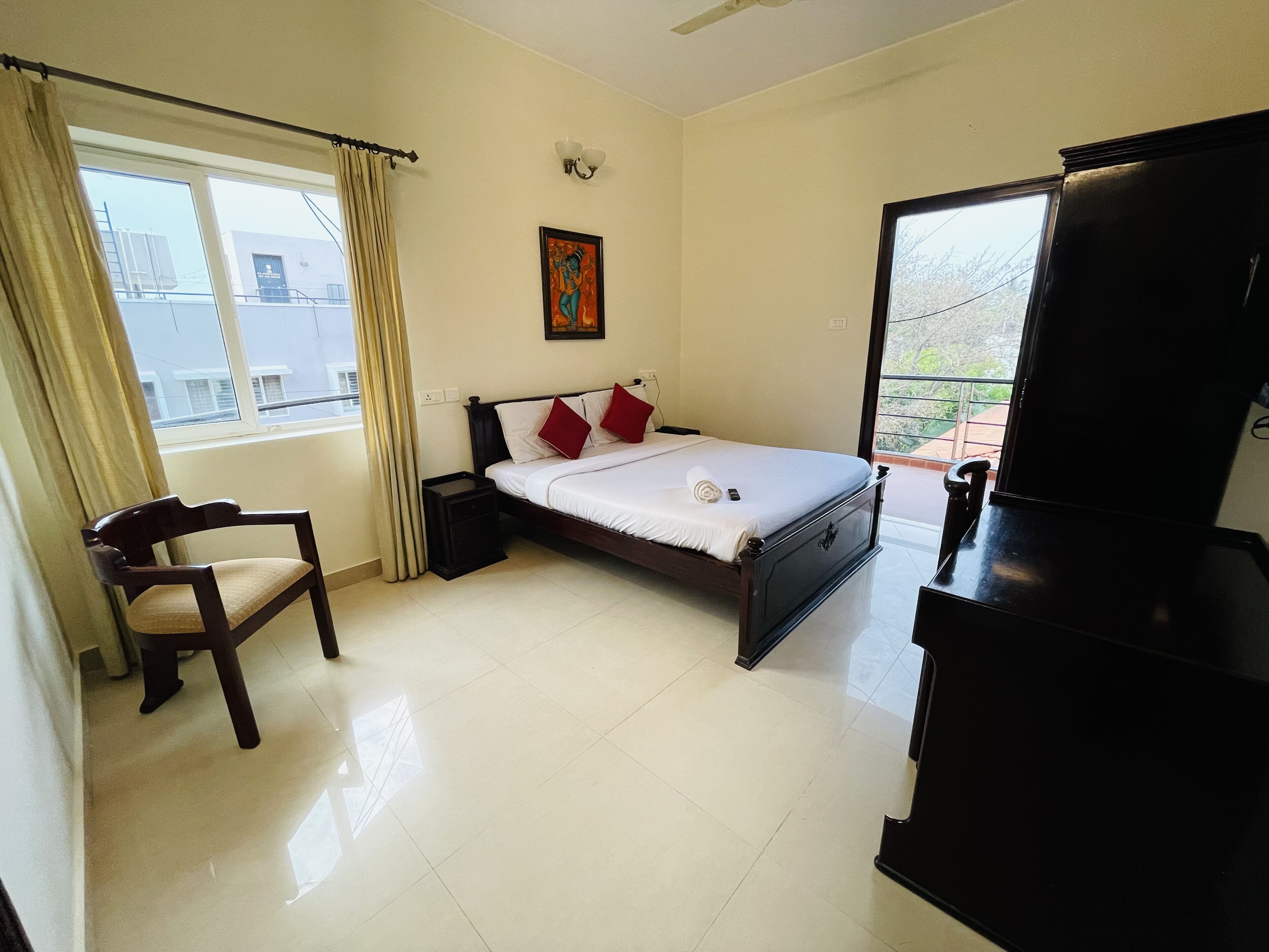 A bedroom with a bed, a chair, a small table, a TV, and a window with curtains.