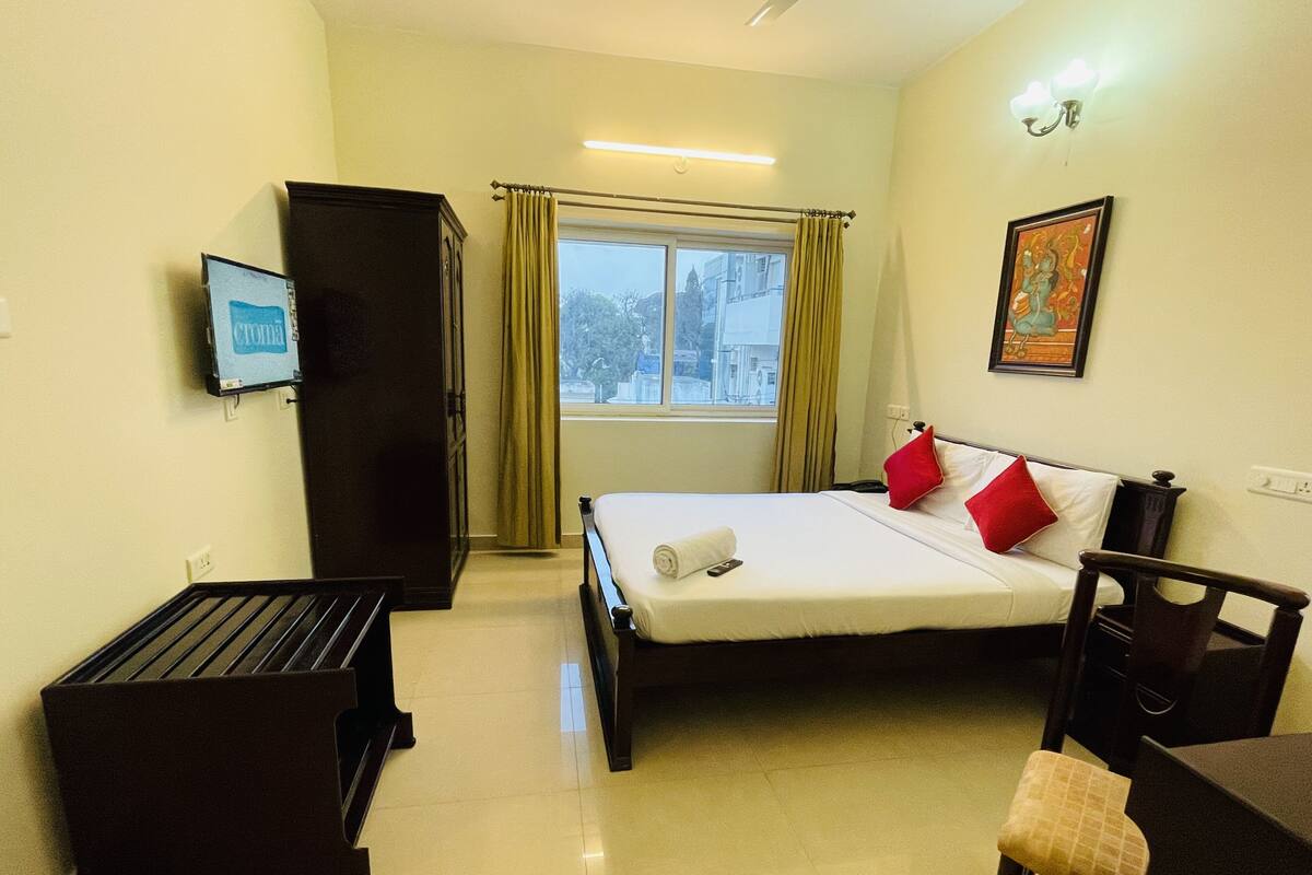 Hotelkamer met een bed, bureau, garderobe, raam met gordijnen, een aan de muur bevestigde televisie en een schilderij.