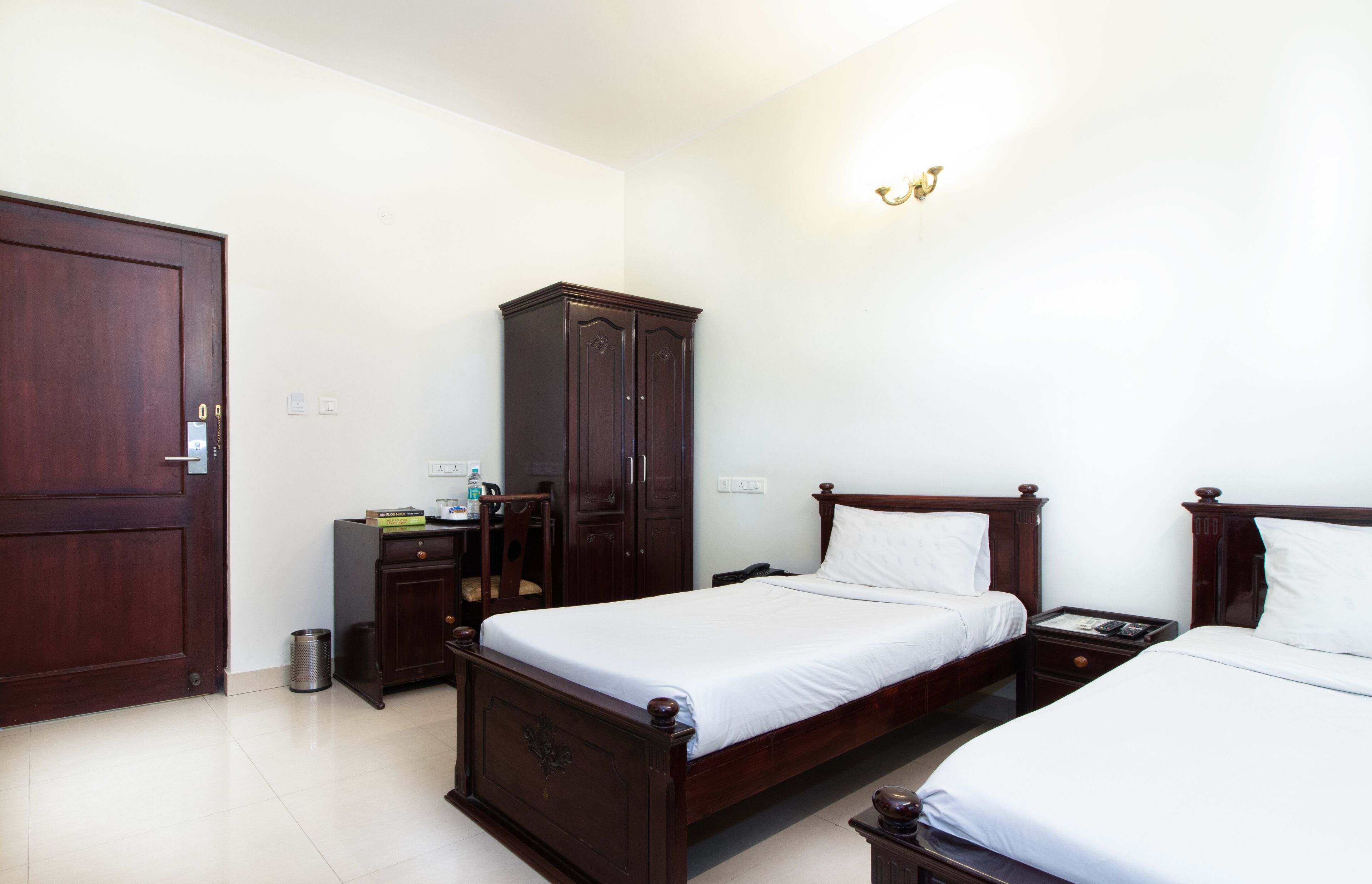 A bedroom with two single beds, a wardrobe, a desk, and a trash bin.