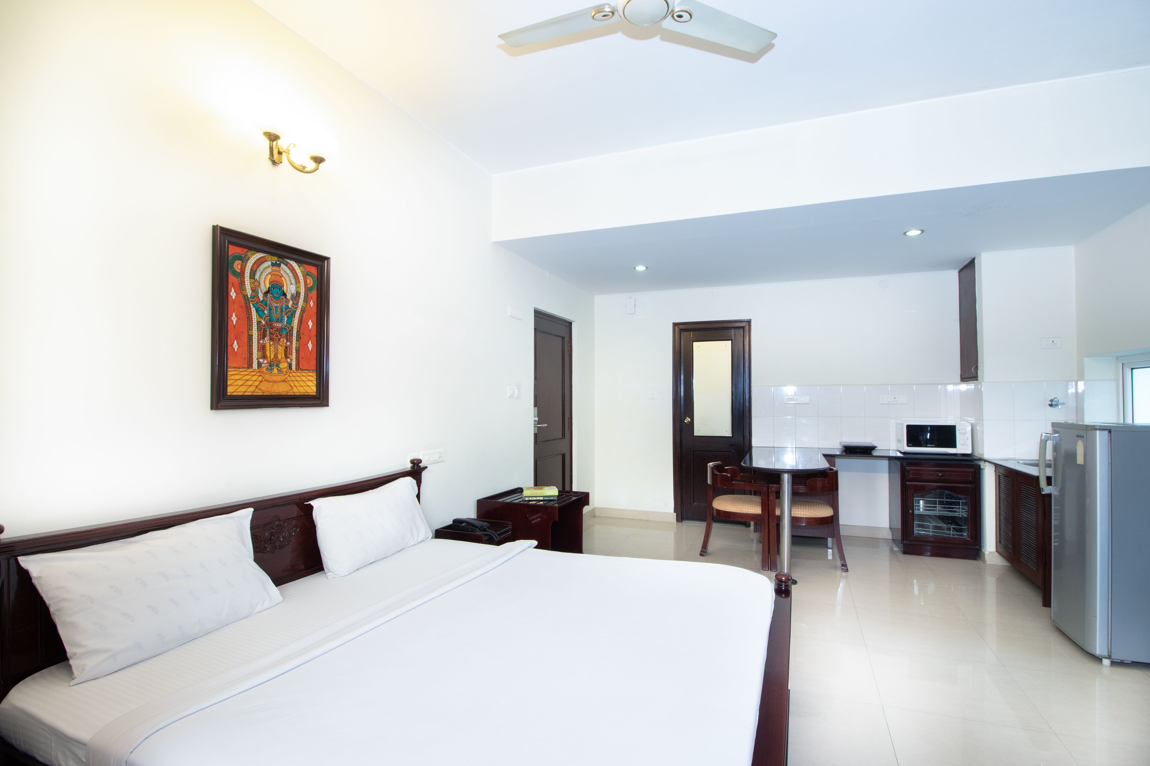 A hotel room with a large bed, a desk, a chair, a microwave, and a refrigerator.