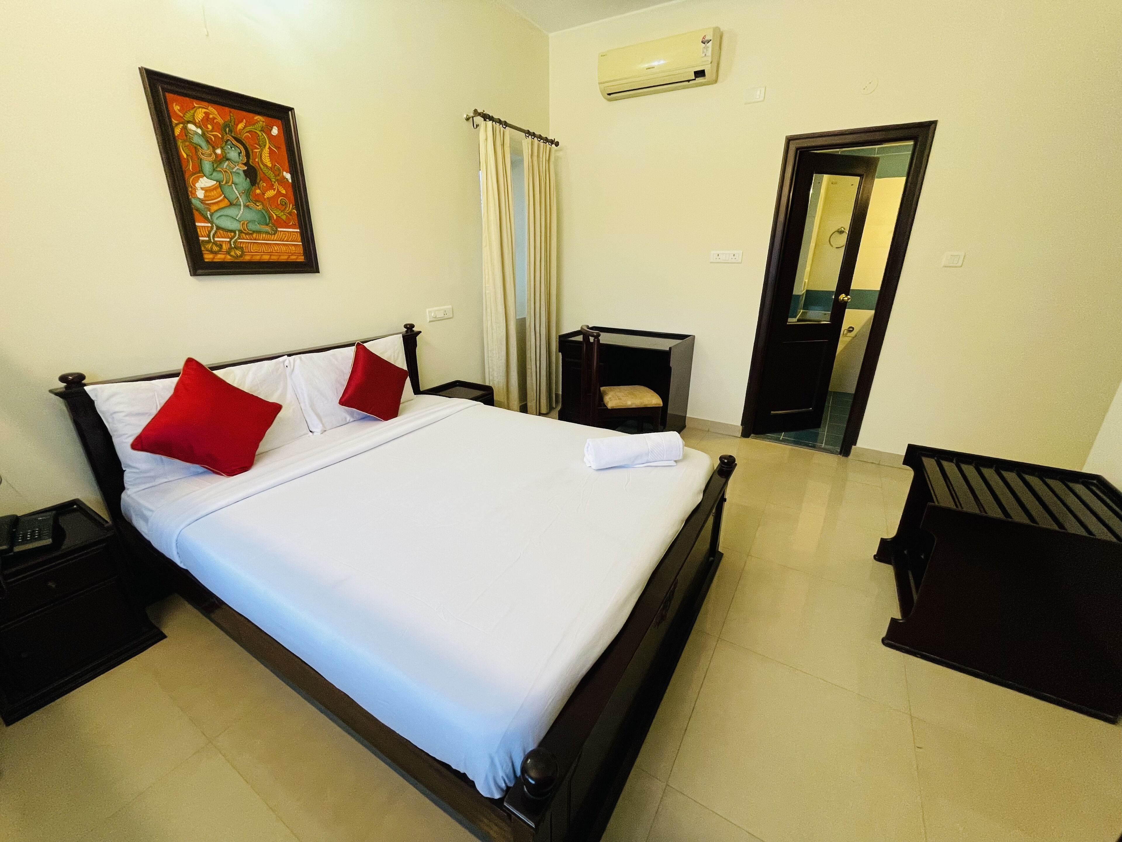 A neatly made bed with white and red pillows, a small bedside table, and a wall-mounted air conditioner.