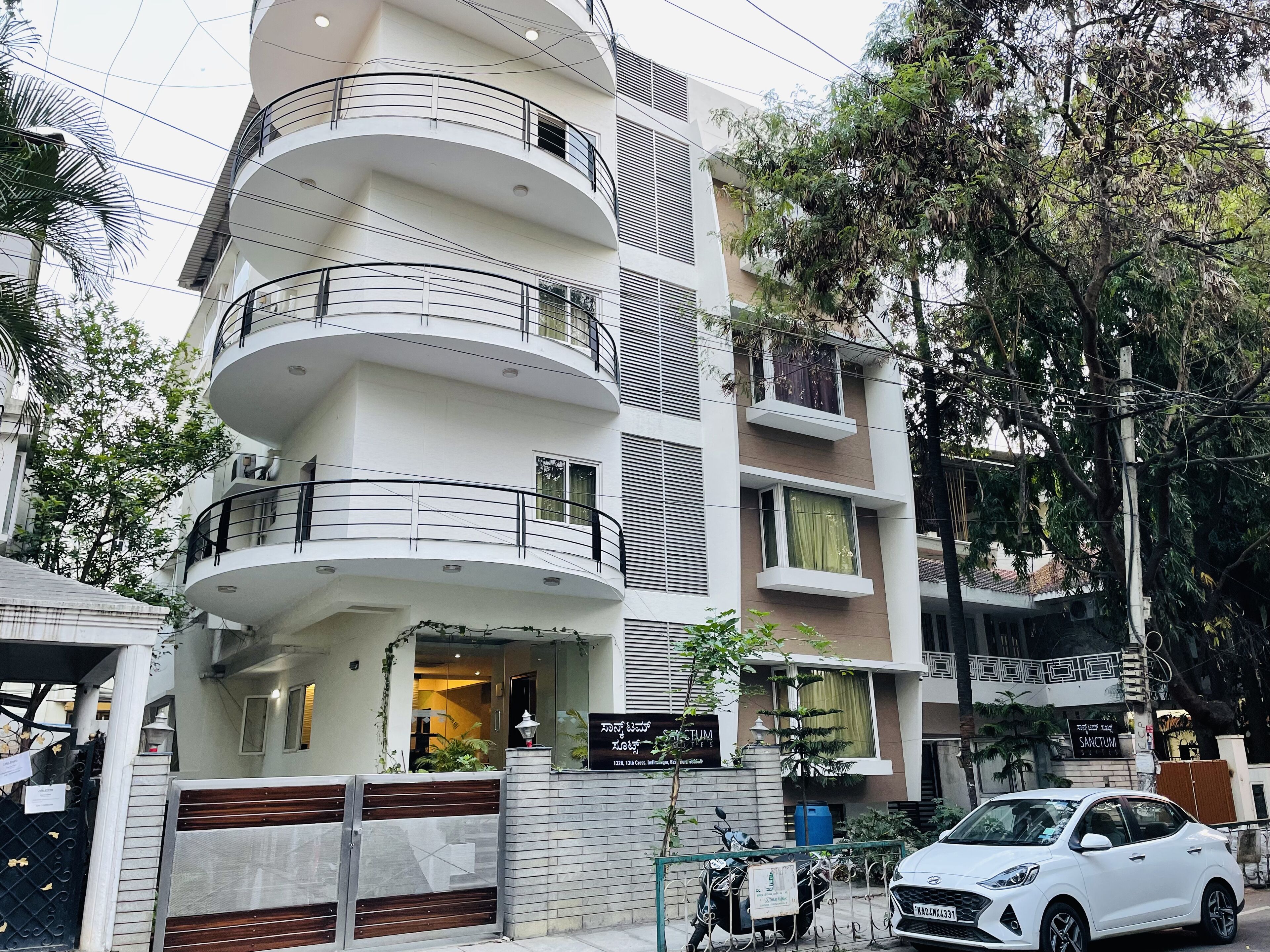 Un edificio residencial de varios pisos con balcones, entrada protegida por una reja y un coche estacionado.